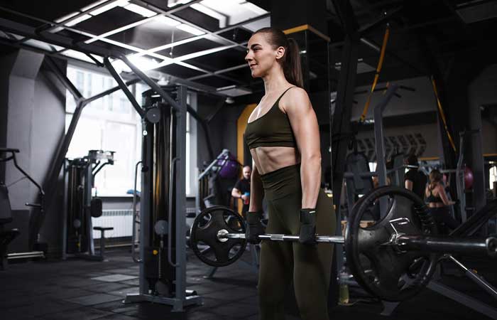 An athletic woman performing sumo deadlifts with a heavy barbell.